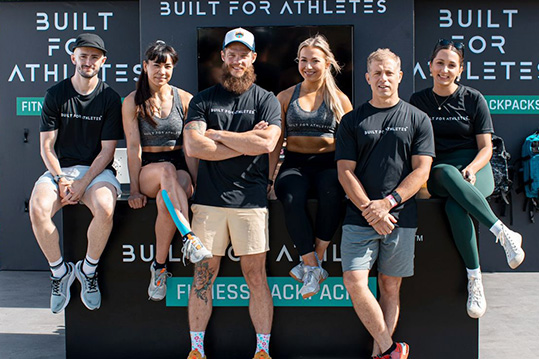 coach with 5 other people with the logo of "Built for athlets" behind them